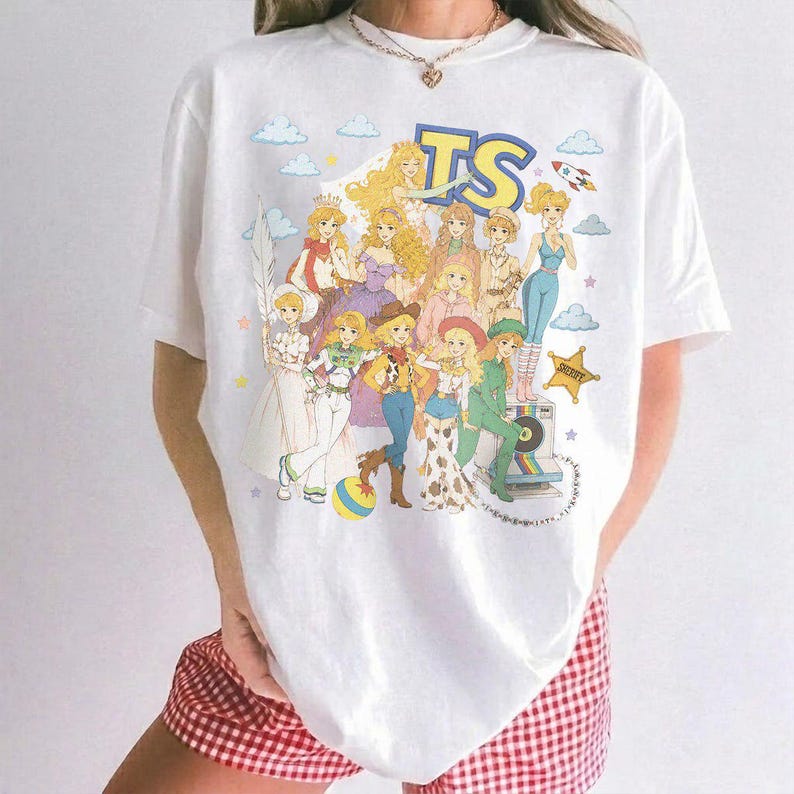 May include: A white short-sleeve t-shirt featuring a colorful graphic print of various animated characters in a retro style. The design includes the letters TS at the top, a yellow star, clouds, and a rocket ship, all arranged in a group illustration.