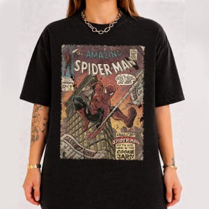 May include: Black t-shirt featuring a vintage comic book cover of Spider-Man. The comic art shows Spider-Man swinging through a city, with text that reads "The Amazing Spider-Man" and "Daily Bugle".