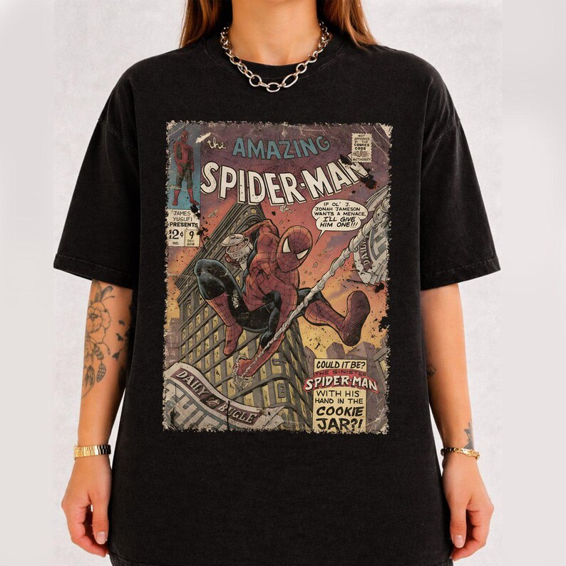 May include: Black t-shirt featuring a vintage comic book cover of Spider-Man. The comic art shows Spider-Man swinging through a city, with text that reads "The Amazing Spider-Man" and "Daily Bugle".