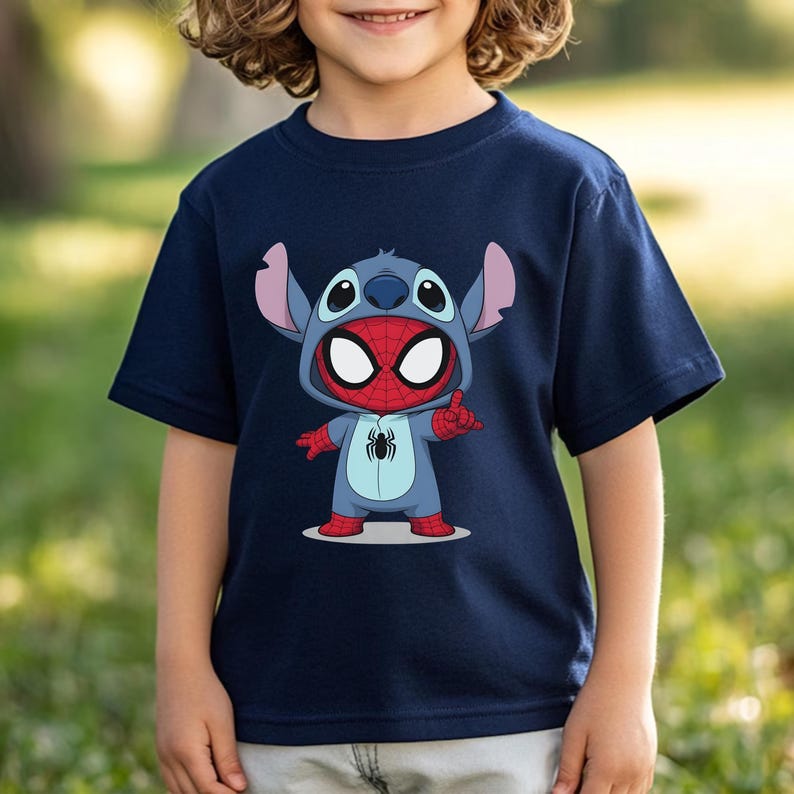 May include: A navy blue short-sleeved t-shirt featuring a graphic print of a character wearing a blue alien costume with large ears and a red and blue spider-themed mask. The character has a black spider emblem on its chest and is making a hand gesture.