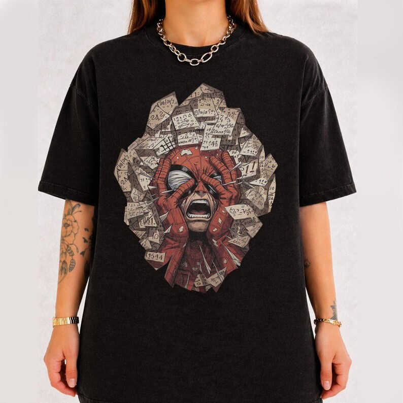 May include: A black short-sleeve t-shirt featuring a graphic print of a red masked character with hands on their head, surrounded by a collage of scattered paper notes with handwritten numbers and mathematical equations in a jagged shape.