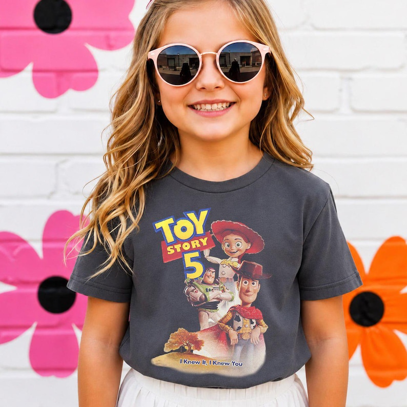 May include: A charcoal gray short-sleeve t-shirt featuring a graphic print of the Toy Story 5 logo with characters Woody, Jessie, and Buzz Lightyear. The text below the characters reads I Knew It, I Knew You. The shirt has a crew neckline.