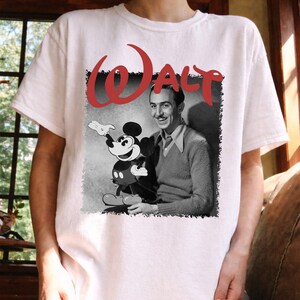 May include: White t-shirt with a black and white image of Walt Disney and Mickey Mouse. The word "WALT" is printed in red above the image. The shirt has a crew neck.