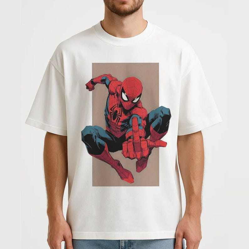 Puede incluir: Una camiseta blanca de manga corta con un estampado gr&aacute;fico del personaje de c&oacute;mic Spider-Man en posici&oacute;n agachada. El personaje lleva un traje rojo y azul con un emblema de ara&ntilde;a negro en el pecho y hace un gesto con una mano.
