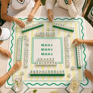 May include: A Mahjong game in progress, featuring a white and green game board with the word "MAHJ" printed on it. The board has a green wavy border and yellow stripes. Green and white tiles are arranged around the board.