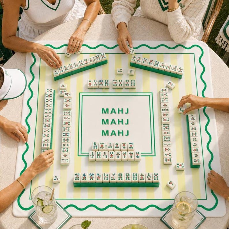 May include: A Mahjong game in progress, featuring a white and green game board with the word "MAHJ" printed on it. The board has a green wavy border and yellow stripes. Green and white tiles are arranged around the board.
