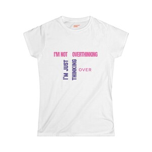 May include: White t-shirt with the text "I'M NOT OVERTHINKING, I'M JUST THINKING OVER" in a gradient of pink and purple. The shirt is a crew neck and appears to be made of a soft material.
