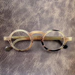 May include: Round-framed spectacles with a light brown and dark brown marbled pattern. The spectacles have a keyhole bridge and a light brown frame. The temples are light brown with a dark brown marbled pattern.