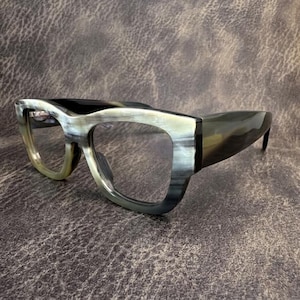 May include: Eyeglasses with a thick, marbled frame in shades of gray, black, and cream. The glasses have a rectangular shape with rounded edges and clear lenses. The temples are dark and sleek, and the overall design is modern and stylish.