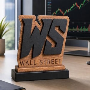 May include: A wooden desk sign featuring the large black letters WS and the text WALL STREET engraved below. The sign has a natural wood grain finish and is mounted on a solid black rectangular base, standing upright on a flat surface.