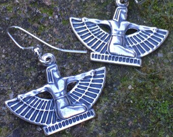 May include: A pair of silver-colored earrings. Each earring features a stylized figure with outstretched wings and arms, kneeling on a rectangular base. The earrings have a hook closure.