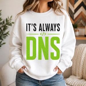 May include: White sweatshirt with the text "IT'S ALWAYS DNS" in black and green. The design includes a coding symbol. The sweatshirt is a casual style.