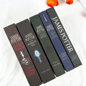 May include: Five hardcover books from the James Potter series by G. Norman Lippert, arranged in a row. The spines are colored in shades of brown, dark green, blue, and black, featuring titles, author names, and graphic illustrations.