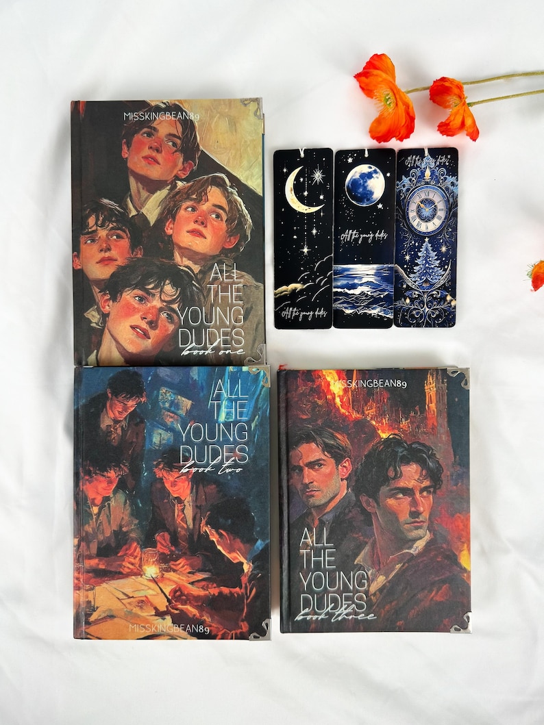 Op de afbeelding: Een verzameling boeken en bladwijzers met de titel "All The Young Dudes". De boekomslagen tonen illustraties van jonge mannen. De bladwijzers hebben hemelse ontwerpen met manen, sterren en een klok. Oranje bloemen zijn op de achtergrond.