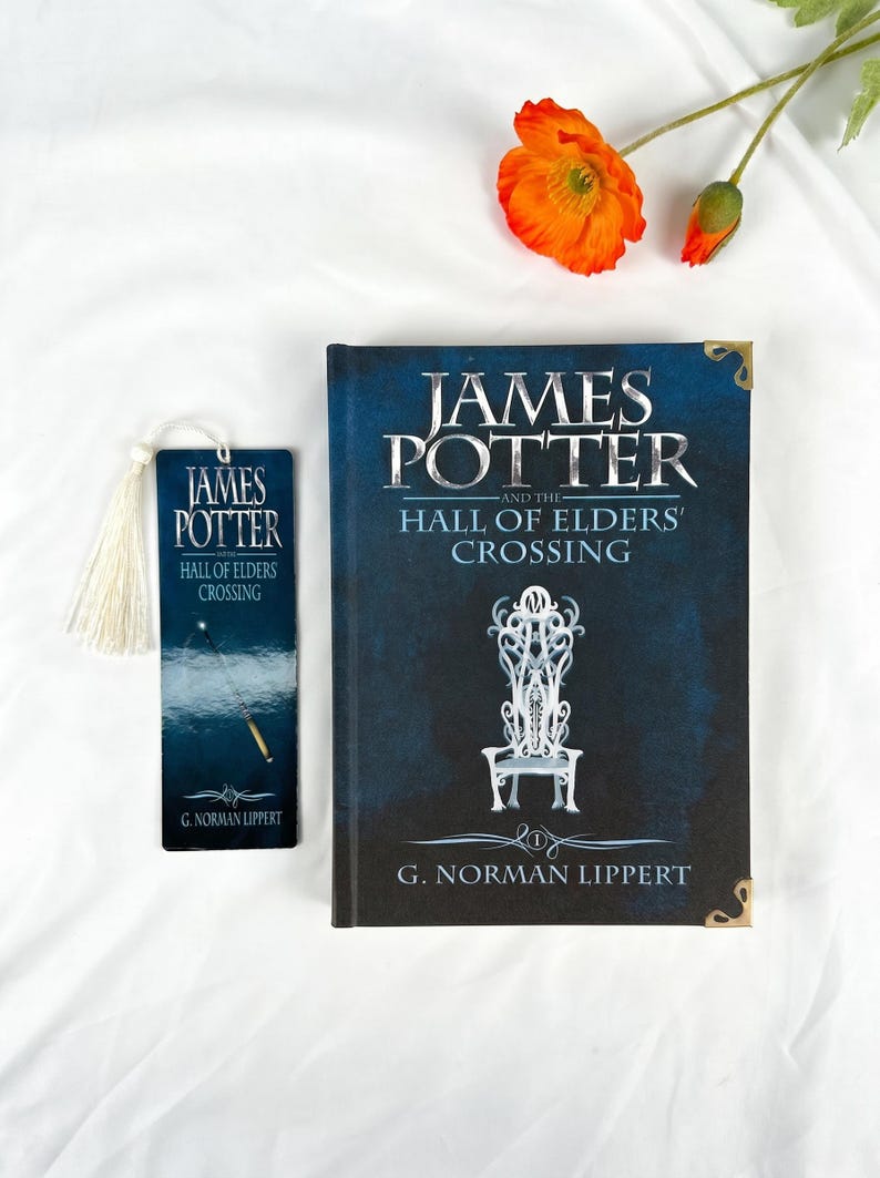 May include: A hardcover book titled James Potter and the Hall of Elders' Crossing by G. Norman Lippert with a dark blue cover featuring a white throne illustration, alongside a matching rectangular bookmark with a white tassel.