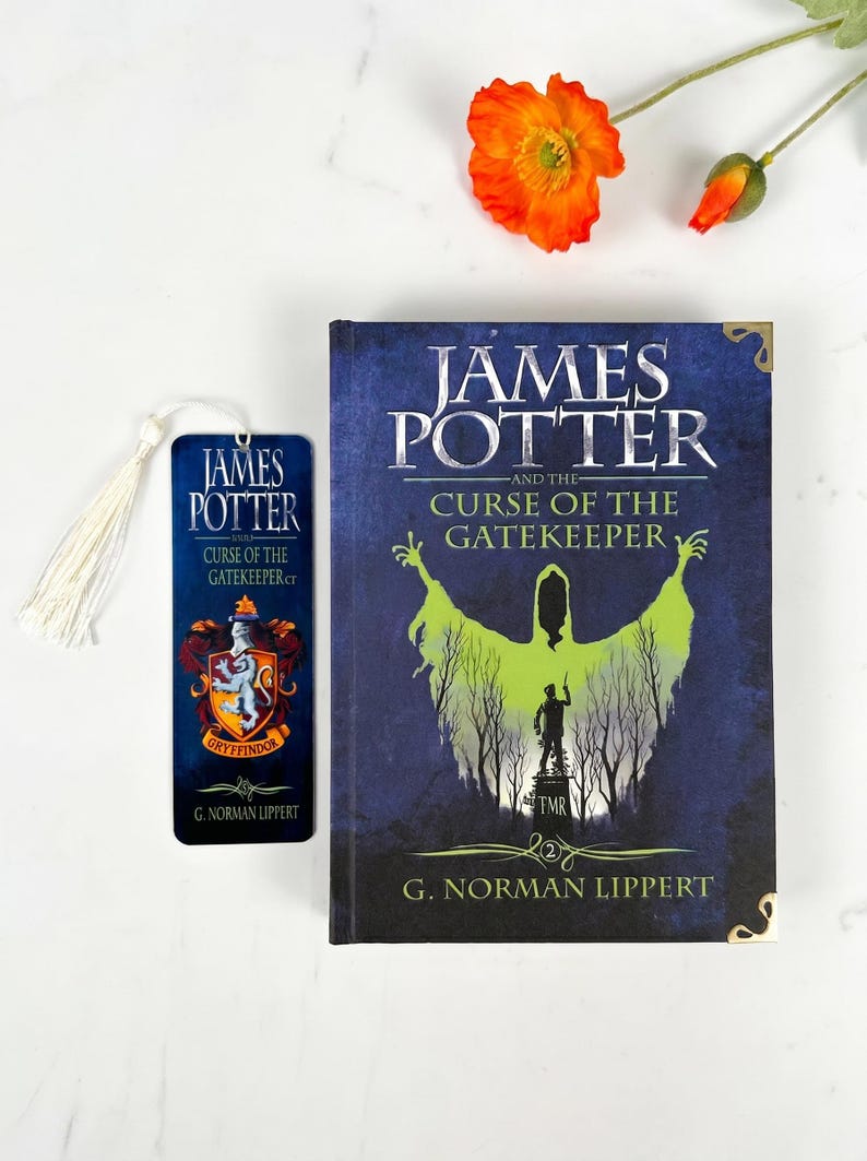 May include: A hardcover book titled James Potter and the Curse of the Gatekeeper by G. Norman Lippert with a blue cover featuring a green silhouette and a matching bookmark with a white tassel and a Gryffindor crest, accompanied by an orange flower.