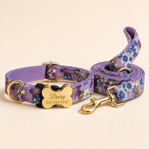 Könnte beinhalten: Ein violettes Haustierhalsband und eine passende Leine mit einem Blumenmuster aus blauen und weißen Blüten. Das Halsband enthält eine goldfarbene, knochenförmige Marke mit der Gravur Daisy und der Telefonnummer 617-555-0153 sowie goldene Beschläge.