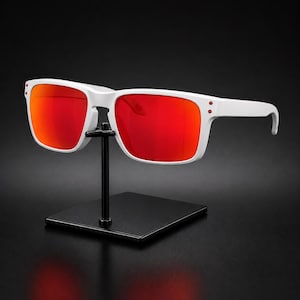 May include: Sunglasses with a matte white frame and vibrant red mirrored lenses. The rectangular frames feature two small red rivets on each outer corner near the temples, providing a distinct contrast against the white plastic material.