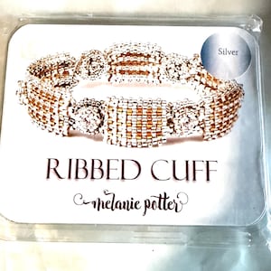 May include: A beaded cuff bracelet featuring alternating vertical stripes of metallic silver and gold beads, presented on a white display card labeled RIBBED CUFF and melanie potter, with a circular Silver indicator in the upper right corner.