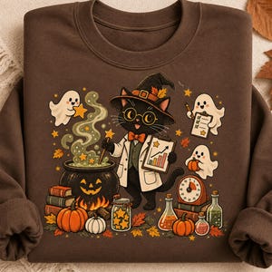 Puede incluir: Una sudadera de manga larga de color marrón oscuro con un gráfico de un gato negro con sombrero de bruja, gafas y bata blanca. El gato sostiene una varita y un gráfico. Rodeando al gato hay fantasmas, un caldero de calabaza, calabazas, libros y frascos.