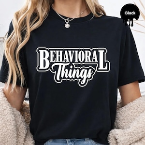 May include: Black t-shirt with the white text "BEHAVIORAL Things" in a bold, outlined font. The shirt is a crew neck style and appears to be made of a soft material. The word "Black" is written in a black circle in the upper right corner.