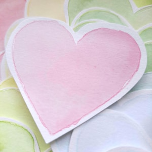 May include: A collection of heart-shaped paper cutouts featuring watercolor washes in various pastel shades including pink, light green, yellow, and blue. Each heart has a white border and a textured surface, layered to show multiple pieces.