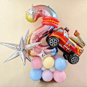 May include: A festive balloon arrangement featuring a large number 2 in pink and silver, a red fire truck balloon, and a cluster of pastel-colored balloons. Includes star-shaped and round balloons, perfect for a birthday celebration.