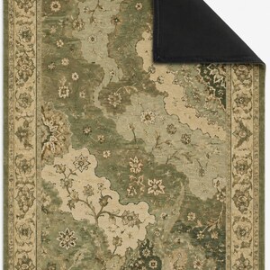 Op de afbeelding: Een rechthoekig vloerkleed met een saliegroen en cr&egrave;mekleurig bloemenpatroon en een decoratieve rand. Het kleed heeft een omgevouwen hoek die een effen zwarte onderkant laat zien. Het ontwerp bevat gedetailleerde botanische motieven en ranken.
