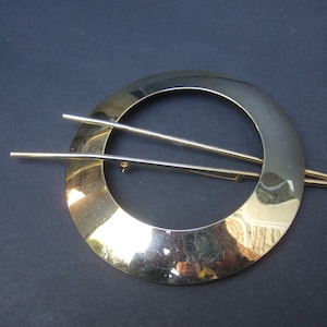 May include: A gold-toned metal hair clip with a circular design. The clip has two thin, straight bars that extend from the circle.