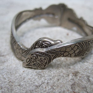 Puede incluir: Un brazalete de serpiente de plata con un diseño intrincado en relieve.