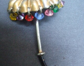 May include: A silver-toned umbrella brooch with a black handle and colorful crystal accents.
