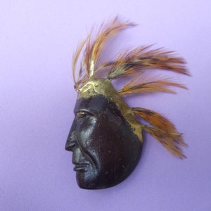 May include: A wooden Native American profile with a gold painted headdress and feathers. The profile is carved in detail and has a dark brown finish.