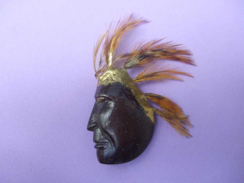 May include: A wooden Native American profile with a gold painted headdress and feathers. The profile is carved in detail and has a dark brown finish.