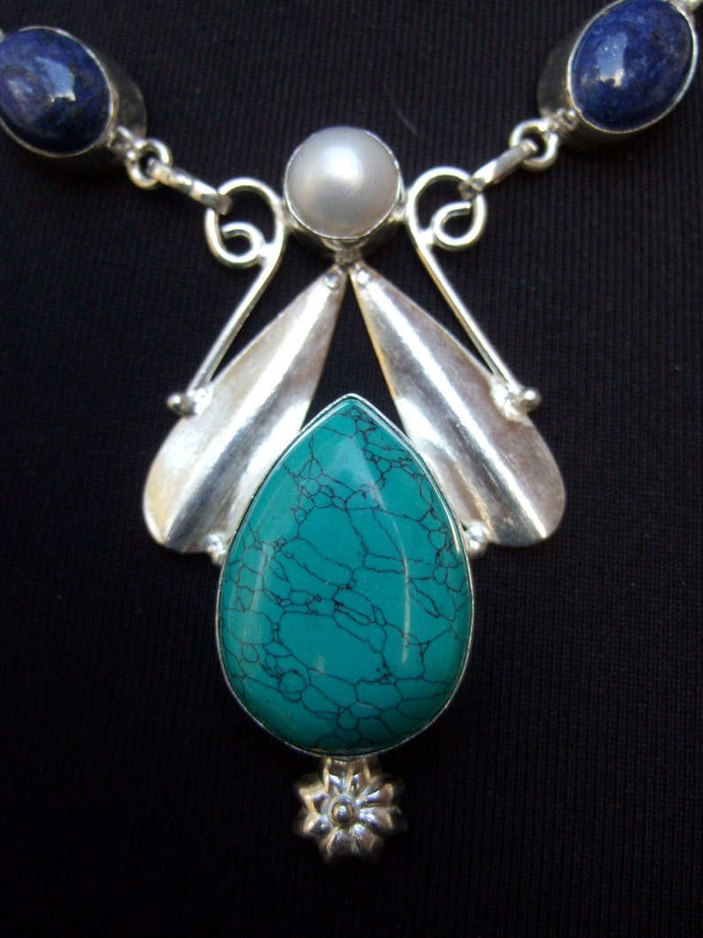 May include: A silver necklace with a turquoise pendant, a pearl, and two lapis lazuli stones.