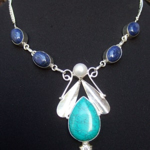 May include: A silver necklace with a turquoise pendant and blue oval stones. The pendant features a silver flower design and a pearl.