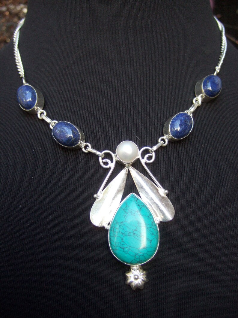 May include: A silver necklace with a turquoise pendant and blue oval stones. The pendant features a silver flower design and a pearl.