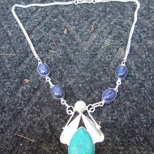 May include: A silver necklace with a turquoise pendant and blue gemstone accents. The pendant is shaped like a stylized butterfly with a pearl in the center.