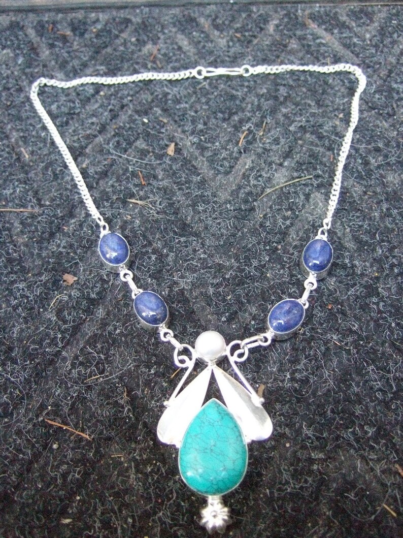 May include: A silver necklace with a turquoise pendant and blue gemstone accents. The pendant is shaped like a stylized butterfly with a pearl in the center.