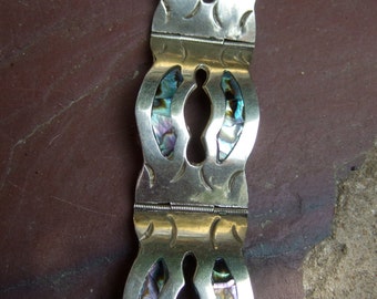 May include: Silver bracelet with a decorative design featuring abalone shell inlay. The bracelet has a hinged clasp.