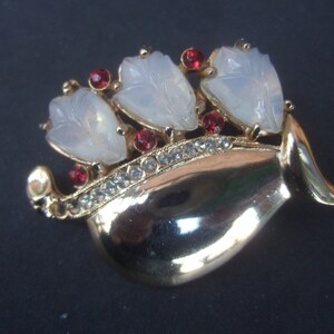 May include: Gold tone brooch with three white flower-shaped stones and red rhinestones. The brooch is shaped like a vase.