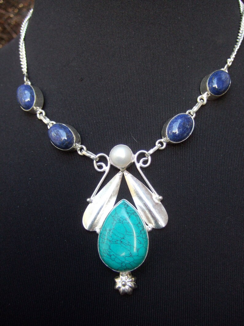 May include: A silver necklace with a turquoise pendant and blue oval stones. The pendant features a silver design with a pearl accent.