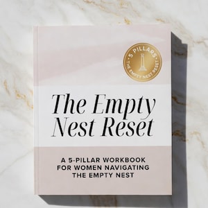 Puede incluir: Un libro titulado "The Empty Nest Reset" con una cubierta rosa pálido y blanca. El título está en negrita, con el texto "A 5-PILLAR WORKBOOK FOR WOMEN NAVIGATING THE EMPTY NEST" debajo. También es visible un sello dorado con las palabras "The Empty Nest Reset".