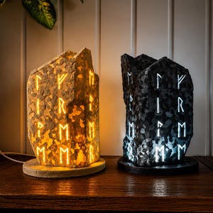 Peut inclure: Deux lampes verticales en forme de pierre avec des bords irréguliers et des runes gravées. La lampe de gauche émet une lueur jaune chaude, tandis que celle de droite émet une lumière blanche froide. Elles reposent sur des bases circulaires.