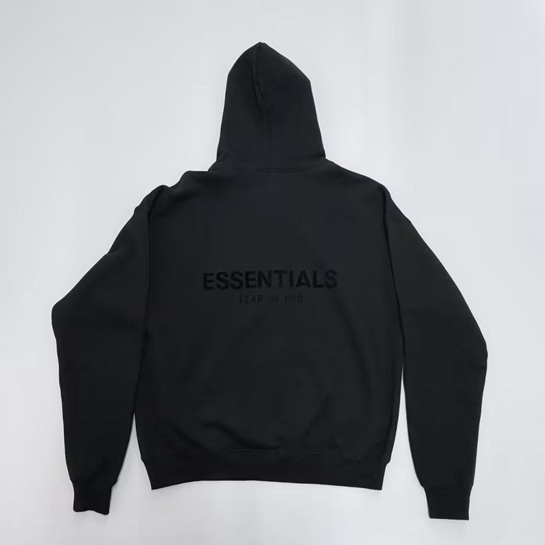 May include: Black hoodie with the word "ESSENTIALS" printed on the back. The hoodie has a hood and long sleeves. The text "FEAR OF GOD" is printed below "ESSENTIALS".