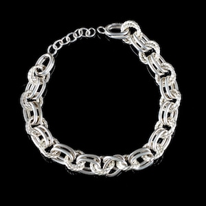 Puede incluir: Un collar de cadena en tono plateado que presenta una serie de eslabones ovalados entrelazados. El diseño alterna entre eslabones de metal liso y pulido y eslabones texturizados con forma de cuerda trenzada. Incluye una pequeña cadena extensora.