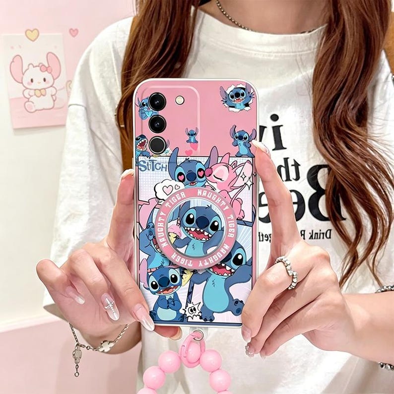 Pu&ograve; includere: Custodia per telefono rosa con il personaggio Stitch di Lilo & Stitch. Il design presenta Stitch in varie pose, con la scritta "Naughty Tiger". Include un anello di supporto e un cinturino da polso con perline rosa.