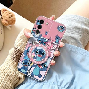 Pu&ograve; includere: Custodia per telefono rosa con un personaggio dei cartoni animati blu. La custodia presenta un'impugnatura pop-up con le parole "Naughty Tiger" e diverse immagini del personaggio. La custodia ha un bordo argentato e un ritaglio per la fotocamera.