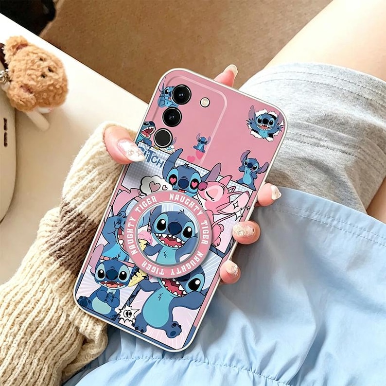 Pu&ograve; includere: Custodia per telefono rosa con un personaggio dei cartoni animati blu. La custodia presenta un'impugnatura pop-up con le parole "Naughty Tiger" e diverse immagini del personaggio. La custodia ha un bordo argentato e un ritaglio per la fotocamera.