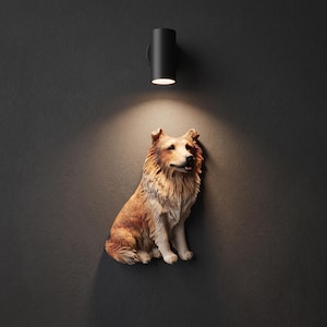 May include: A wall-mounted sculpture of a sitting collie dog with brown and white fur, positioned directly beneath a cylindrical black wall light fixture that casts a warm, downward-facing beam of light onto the dog figure.