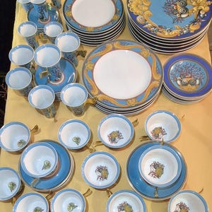 Puede incluir: Juego de vajilla de porcelana fina con diseño azul y dorado. El juego incluye platos, platillos, tazas y jarrones altos. Los platos tienen un centro blanco con un borde azul y dorado. Las tazas y jarrones son azules con detalles dorados.